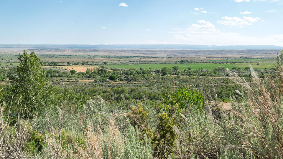 A green, irrigated valley surrounded by rugged badlands.