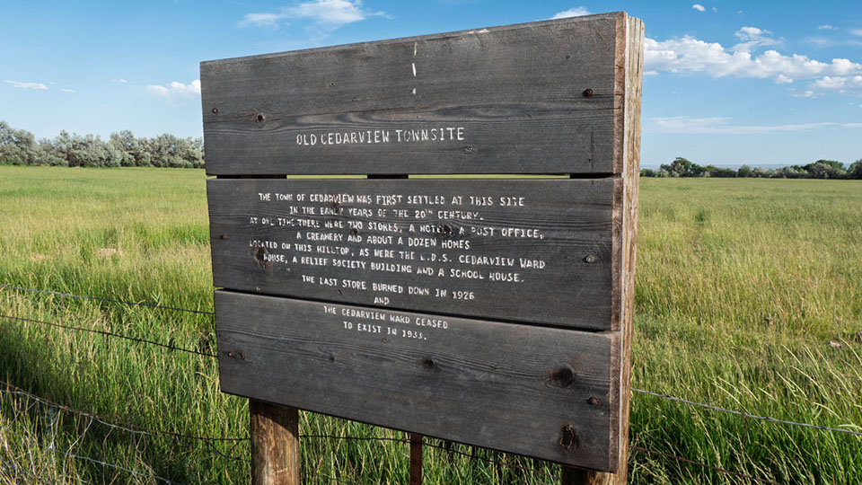 A wooden historical sign in front of a grassy, green field.