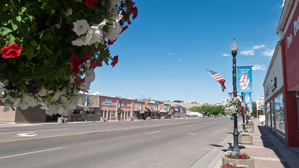 Old store fronts on a street lined with hanging baskets of flowers.
