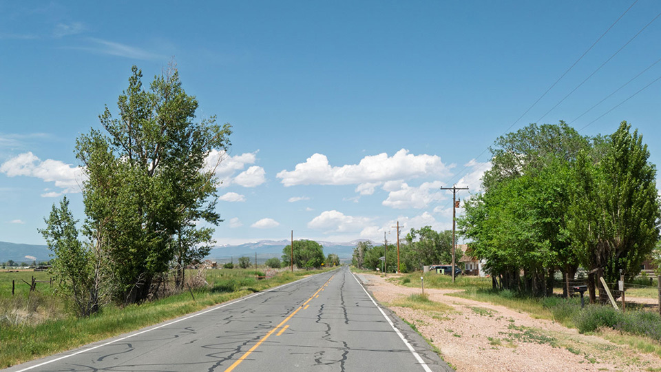 A country road lined with fields and High Uinta peaks in the background