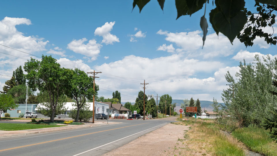 Town of Neola with store and houses, set against blue sky, mountains, and cottonwood trees.