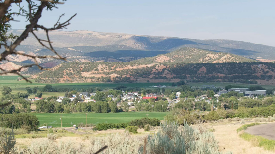 A view of a green valley surrounded by red hills dotted with juniper trees.